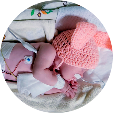 Noworodek w różowej czapce z podłączonymi elektrodami podczas monitorowania czynności życiowych i EEG.