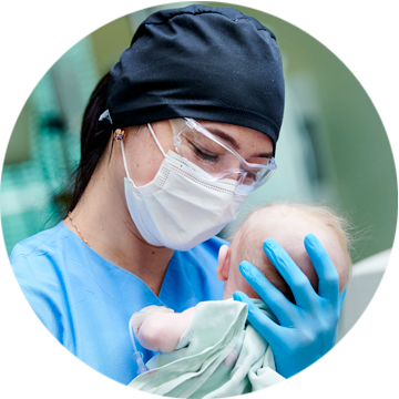 Lekarz specjalista w maseczce i goglach ochronnych trzyma noworodka na rękach.