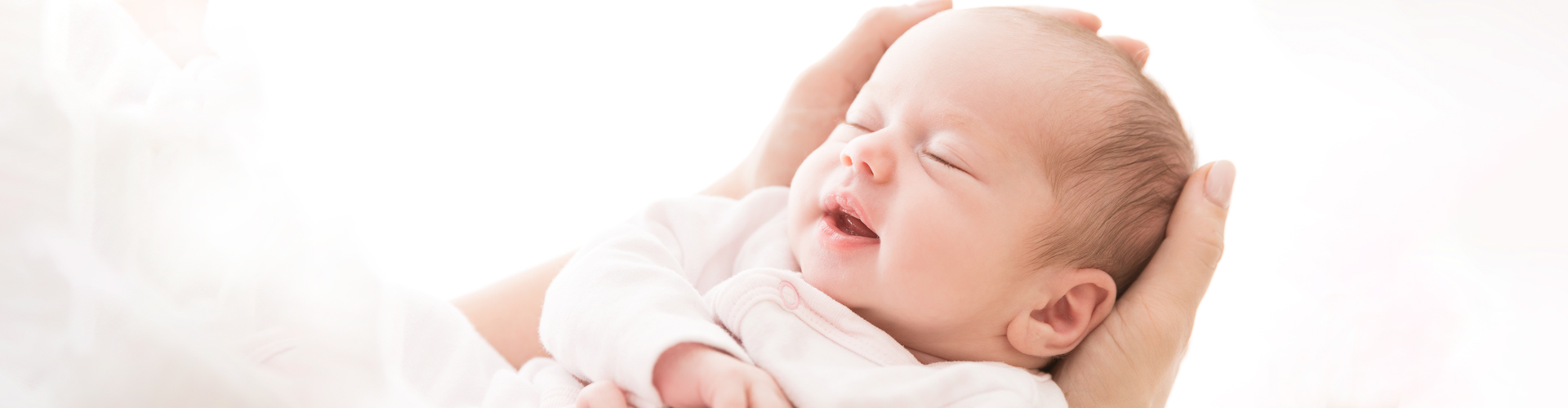 Śpiący noworodek trzymany w dłoniach na jasnym tle – baner diagnostyki EEG noworodka.