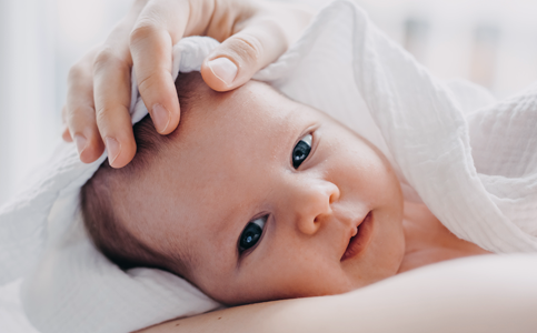 Noworodek owinięty w biały kocyk z czułą dłonią rodzica na główce – diagnostyka EEG noworodka.